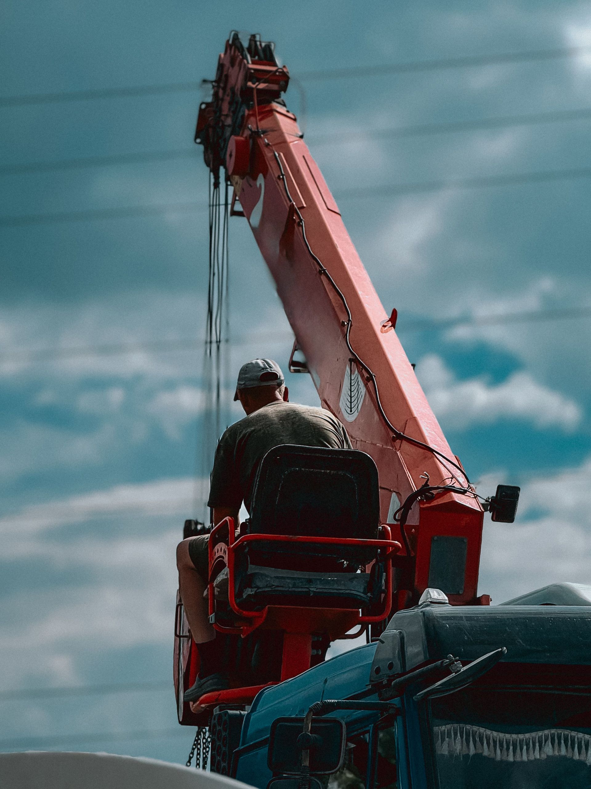 A crane operator managing heavy machinery outdoors with a backdrop of a blue sky and clouds.